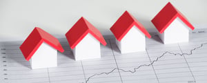 Vier modelwoningen met rode daken staan op een financieel diagram dat een stijgende curve laat zien – een symbool voor de kapitaalmarkt, investeringen en een positieve bedrijfsontwikkeling.
