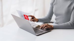 Een persoon gebruikt een laptop en tikt op een holografisch beveiligingsscherm met een rood slotje – Key Visual voor IT-beveiligingsdiensten.