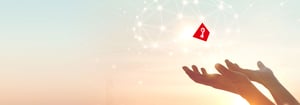 Symbolisches Bild: Hände halten einen roten Würfel mit Schlüsselsymbol in einem Netzwerk aus Lichtpunkten – Darstellung für sichere und flexible Cloud Services von DATAGROUP